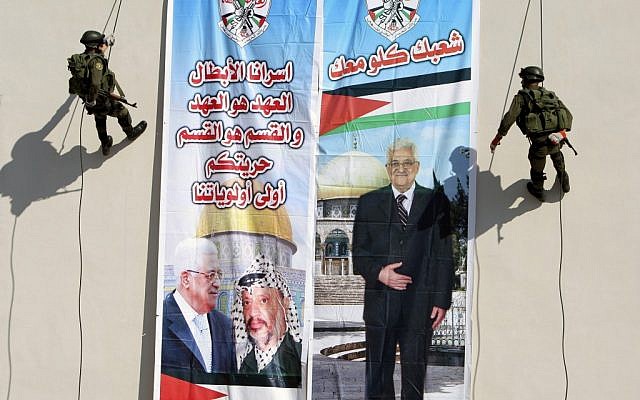 Palestinian security officers slide down a building next to a banner of PA President Mahmoud Abbas with Yasser Arafat, in the West Bank town of Jenin in 2012. Arabic on the left reads "our hero prisoners, the covenant is the covenant and the section is the section, your liberty will stay our first priority," and right, "all your people (are) with you."(photo credit: AP/Mohammed Ballas) Palestinian security officers slide down a building next to a banner of PA President Mahmoud Abbas with Yasser Arafat, in the West Bank town of Jenin in 2012. Arabic on the left reads "our hero prisoners, the covenant is the covenant and the section is the section, your liberty will stay our first priority," and right, "all your people (are) with you."(photo credit: AP/Mohammed Ballas)