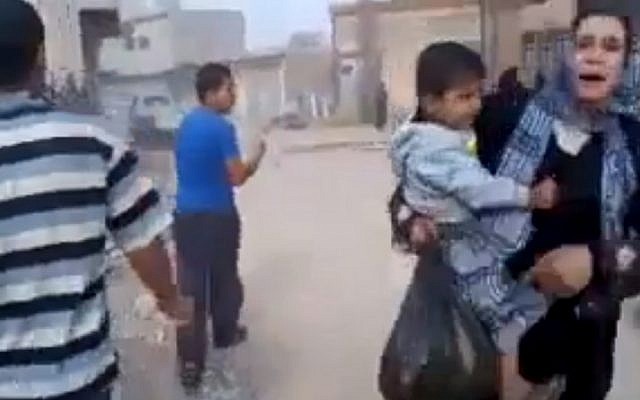 This image taken from video obtained by the Associated Press shows a woman carrying a child running away from the scene of shelling in Qouriyeh, Syria on Friday. (AP/Shaam News Network via AP video)