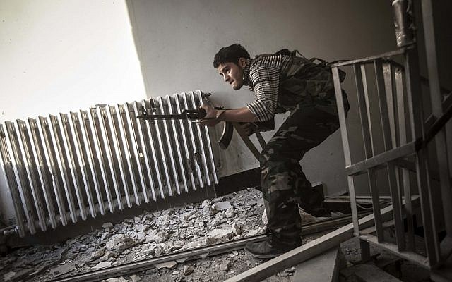 A rebel fighter belonging to the Liwa Al-Fatah takes cover as he aims at an enemy position from a school building during skirmishes with the Syrian army in the nearby Bustan Al-Pasha front line in Aleppo, Syria, on Tuesday, Oct. 30, 2012.(photo credit: Narciso Contreras/AP)