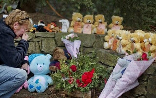 Cheryl Girardi kneels beside 26 teddy bears, each representing a victim of the Sandy Hook Elementary School shooting, at a sidewalk memorial, on Sunday in Newtown, Connecticut (photo credit: AP/David Goldman)