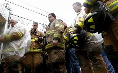 Fire rescue officials pause for a moment of silence at a makeshift memorial near the main road that leads into Sandy Hook Elementary School during a memorial at 9:30 a.m. on Friday in Newtown, Conn. The chiming of bells reverberated throughout Newtown, commemorating one week since the the massacre. (photo credit: AP Photo/Julio Cortez)