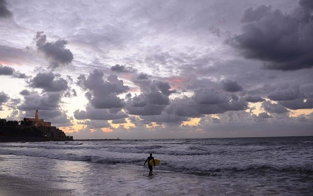 A lone surfer walks along the stormy shoreline of Tel-Aviv (photo credit: Tomer Neuberg/Flash90)