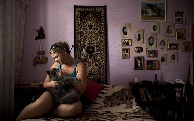 Alexandra Bahman, who emigrated to Israel from Moldova in 2006, sits in her bedroom with her cat. Bahman left Moldova with the carpet and photos that now decorate her bedroom walls, in Ashdod. (photo credit: AP Photo/Oded Balilty) 