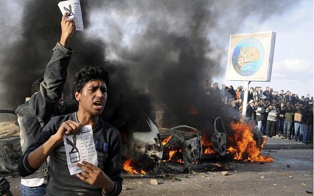 Opponents of Egyptian President Mohammed Morsi hold pamphlets urging a "no vote" on a constitutional referendum as cars burn during clashes between supporters and opponents of President Mohammed Morsi in Alexandria, Egypt, on on Friday, Dec. 14, 2012. (photo credit: AP)