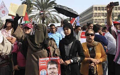 A supporter of Egyptian President Mohammed Morsi holds a Quran and a poster of the president at a rally in front of Cairo University on Saturday. (photo credit: AP/Thomas Hartwell)