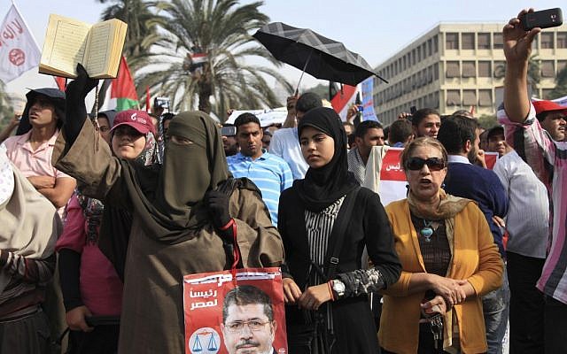 A supporter of Egyptian President Mohammed Morsi holds a Quran and a poster of the president at a rally in front of Cairo University on Saturday. (photo credit: AP/Thomas Hartwell) A supporter of Egyptian President Mohammed Morsi holds a Quran and a poster of the president at a rally in front of Cairo University on Saturday. (photo credit: AP/Thomas Hartwell)