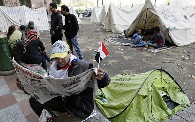 An Egyptian protester reads the newspaper as other sit next to their tents in Tahrir Square in Cairo, Egypt, Sunday, Dec. 9, 2012 (photo credit: AP/Hassan Ammar)