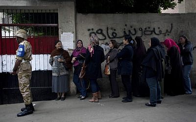 An Egyptian soldier stands guard outside a polling center as women stand in line to cast their votes during a referendum on a disputed constitution drafted by Islamist supporters of President Mohammed Morsi, in Cairo, Egypt, on Saturday, December. 15, 2012. (photo credit: AP Photo/Nasser Nasser)