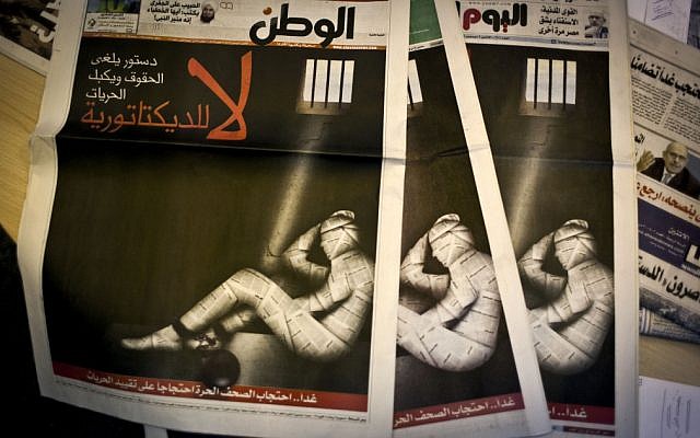 Copies of Egypt’s most prominent newspapers running black background front pages with Arabic text that reads, 'No to dictatorship. Tomorrow, free newspapers will... protest freedom's restrictions' and a picture of a man wrapped in newspaper with his feet cuffed, at the editorial room of Al Masry Al Youm daily newspaper in Cairo on Monday, December 3, 2012. (photo credit: Nasser Nasser/AP)