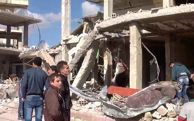 Syrian civilians stand in front of a building destroyed by a car bomb in Qatana, southwest of Damascus on December 13, 2012. (photo credit: AP/SANA)