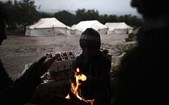 Syrians who fled their homes with their families gather around a fire to warm themselves at a makeshift vegetable store in a camp for displaced persons in the village of Atmeh, Syria in December. (photo credit: AP/Muhammed Muheisen)