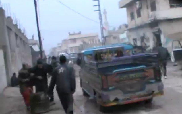 Rebel fighters rush to the scene of a Syrian airstrike on a bakery (at right) in Halfaya, where more than 60 people were reported killed on Sunday. (photo credit: image capture from YouTube video) Rebel fighters rush to the scene of a Syrian airstrike on a bakery (at right) in Halfaya, where more than 60 people were reported killed on Sunday. (photo credit: image capture from YouTube video)