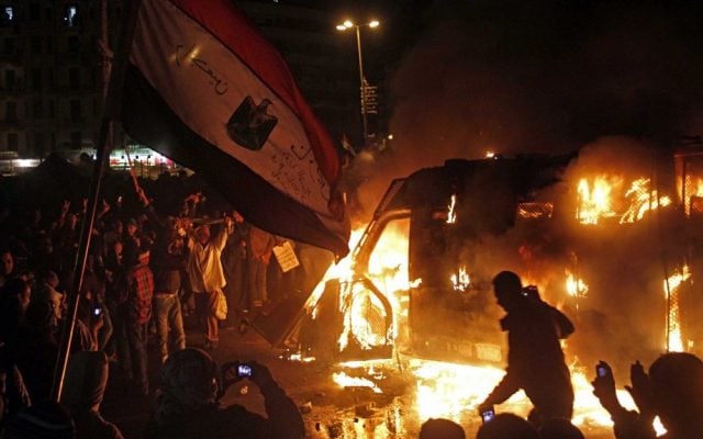Egyptian protesters and a burning state security armored vehicle that demonstrators commandeered, brought to Tahrir Square and set alight, January 28 (photo credit: Mostafa El Shemy/AP)