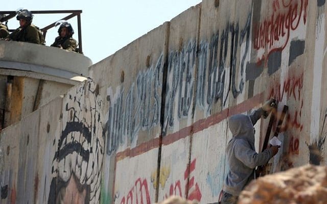 An illustrative photo of an activist painting graffiti on the security barrier during a protest near the Qalandiya checkpoint between Ramallah and Jerusalem. (photo credit: Issam Rimawi/Flash90)