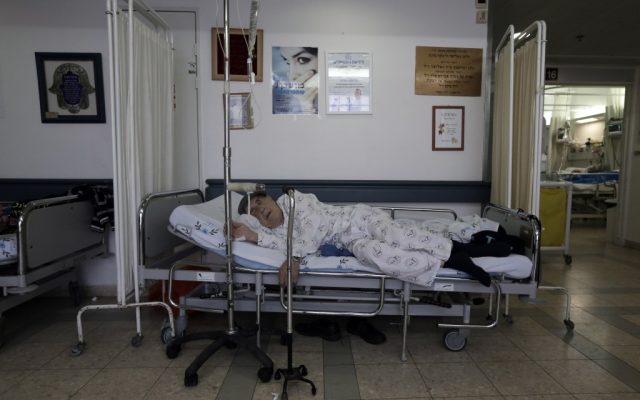 Overcrowding at hospitals has forced many patients to lie on beds in the corridors, like this man at Barzilai Hospital in Ashkelon on Monday. (photo credit: Tsafrir Abayov/Flash90)