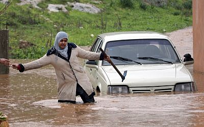 A Palestinian woman passes keys to a person on the other side of a flooded road in the West Bank city of Jenin, on Tuesday, Jan. 8 (photo credit: AP/Mohammed Ballas) A Palestinian woman passes keys to a person on the other side of a flooded road in the West Bank city of Jenin, on Tuesday, Jan. 8 (photo credit: AP/Mohammed Ballas)