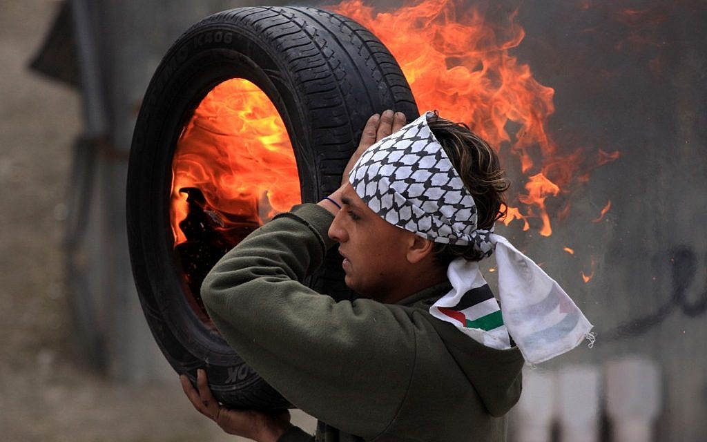 A Palestinian protester holds a burning tire during clashes with Israeli forces in the Qalandia refugee camp (photo credit: Issam Rimawi/Flash90)