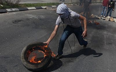 A Palestinian protester rolls a burning tire toward Israeli soldiers during an earlier clash, next to Ofer prison, near the West Bank city of Ramallah (photo credit: Issam Rimawi/Flash90)