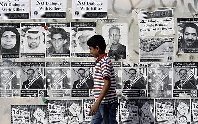 A Bahraini boy walks by a wall with signs in English and Arabic objecting to a government-mediated dialogue between opponents and supporters of the Bahraini monarchy in Sitra, Bahrain, on Saturday, Feb. 9, 2013. (photo credit:AP/Hasan Jamali)