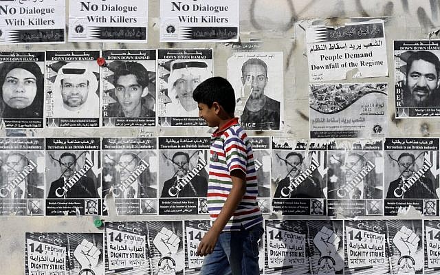 A Bahraini boy walks by a wall with signs in English and Arabic objecting to a government-mediated dialogue between opponents and supporters of the Bahraini monarchy in Sitra, Bahrain, on Saturday, Feb. 9, 2013. (photo credit:AP/Hasan Jamali)