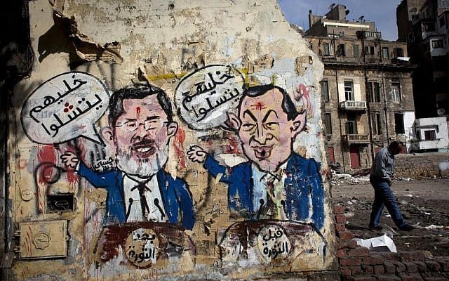 An Egyptian man walks by a mural depicting ousted president Hosni Mubarak, right, and Egyptian President Mohammed Morsi, left, with Arabic that reads 'Before the revolution, let them be amused, after the revolution, let them be paralyzed,' on a wall in Tahrir Square, Cairo, Egypt, Tuesday, Feb. 19, 2013 (photo credit: AP/Nasser Nasser) An Egyptian man walks by a mural depicting ousted president Hosni Mubarak, right, and Egyptian President Mohammed Morsi, left, with Arabic that reads 'Before the revolution, let them be amused, after the revolution, let them be paralyzed,' on a wall in Tahrir Square, Cairo, Egypt, Tuesday, Feb. 19, 2013 (photo credit: AP/Nasser Nasser)