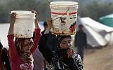 In this Tuesday, Feb. 19, 2013 photo, Syrian refugee girls carry over their heads buckets of water as they walk at Atmeh refugee camp, in the northern Syrian province of Idlib, Syria (photo credit: Hussein Malla/AP)
