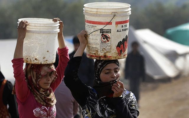 In this Tuesday, Feb. 19, 2013 photo, Syrian refugee girls carry over their heads buckets of water as they walk at Atmeh refugee camp, in the northern Syrian province of Idlib, Syria (photo credit: Hussein Malla/AP) In this Tuesday, Feb. 19, 2013 photo, Syrian refugee girls carry over their heads buckets of water as they walk at Atmeh refugee camp, in the northern Syrian province of Idlib, Syria (photo credit: Hussein Malla/AP)
