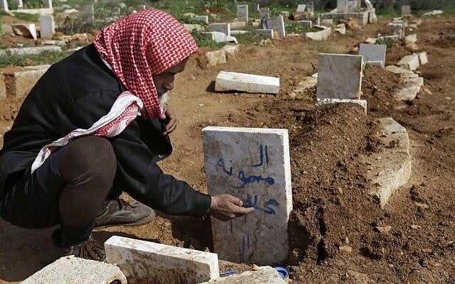 An illustrative photo of a Syrian villager writing the name of his granddaughter (who was killed by an airstrike by Syrian government forces) on her grave near the village of Sarja, in Idlib, Syria, on Sunday. (photo credit: AP/Hussein Malla)