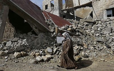 Illustrative photo of a Syrian woman walking past a house destroyed by a government airstrike in Idlib, Syria, on February 25, 2013. (photo credit: AP/Hussein Malla)