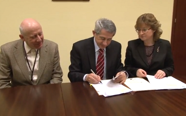 Polish State Archives general director Władysław Stępniak signs Friday's agreement at a ceremony attended by PSA official Ania Krochmal and Jewish Records Indexing representative Krzysztof Malczewsk. (YouTube screenshot)