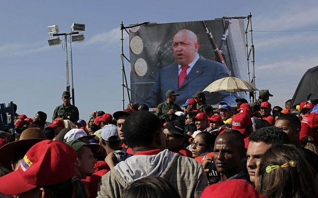 A screen showing a video image of Venezuela's President Hugo Chavez plays in front of the site where Chavez's funeral ceremony will take place as people gather outside the military academy in Caracas, Venezuela, Friday, March 8, 2013. (photo credit: AP/Rodrigo Abd)