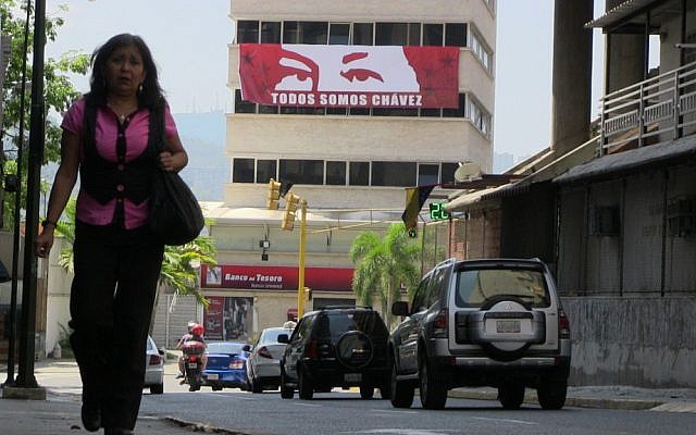 A pedestrian walks underneath a poster showing the eyes of the late leftist leader Hugo Chavez in downtown Caracas. The sign reads, "We are all Chavez." (photo credit: Gil Shefler/JTA) 