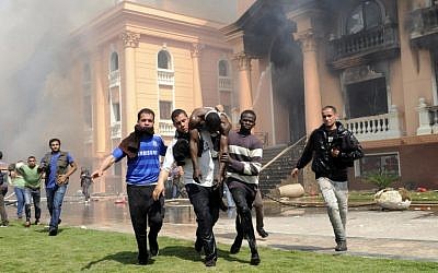An injured security official is carried from a police officers club after protesters set fires following a court verdict in Cairo on Saturday. (photo credit: AP Photo/Mohammed Asad)