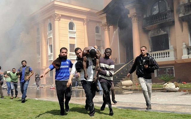 An injured security official is carried from a police officers club after protesters set fires following a court verdict in Cairo on Saturday. (photo credit: AP Photo/Mohammed Asad)