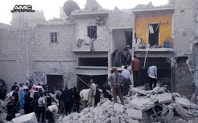 Syrian citizens stand on the rubble of houses that were destroyed by government airstrikes in Aleppo, Syria, earlier this month (photo credit: AP/Aleppo Media Center)