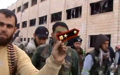 In this Sunday March 3, 2013 image taken from video obtained from the Shaam News Network, which has been authenticated based on its contents and other AP reporting, a Syrian rebel fighters displays an epaulette from a government soldier during a tour of the police academy complex in Khan al-Asal, in the province of Aleppo, Syria. (photo credit: AP/Shaam News Network via AP video)