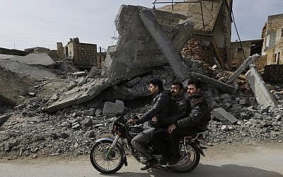 A Syrian drives his motorbike past a house destroyed in a government airstrike, at Jabal al-Zaweya village of Sarjeh, in Idlib, Syria, Monday February 25, 2013 (photo credit: AP/Hussein Mallah)
