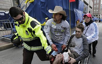An emergency responder and volunteers -- including Carlos Arredondo, in the cowboy hat -- push Jeff Bauman in a wheelchair after he was injured in an explosion near the finish line of the Boston Marathon, Monday, March 15, 2013. (AP/Charles Krupa, File)