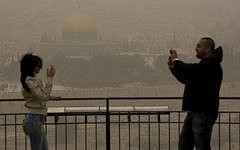 An Arab couple stands atop the Mount of Olives, overlooking towards the walls of the Old City of Jerusalem and the distinctive golden Dome of the Rock, as a sandstorm hits the capital Monday. (photo credit: Yonatan Sindel/Flash90)