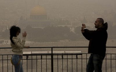 An Arab couple stands atop the Mount of Olives, overlooking towards the walls of the Old City of Jerusalem and the distinctive golden Dome of the Rock, as a sandstorm hits the capital Monday. (photo credit: Yonatan Sindel/Flash90)