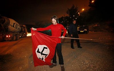 Police watch as Meir Schijveschuurder, whose family members were murdered in a suicide bombing attack at the Sbarro restaurant in Jerusalem in 2001, removes a Nazi flag which he hung in protest on his land outside of Jerusalem.  April 16, 2013. (photo credit: Miriam Alster/Flash90)