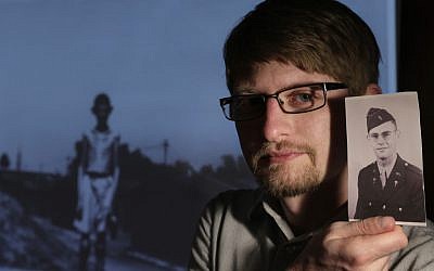 Filmmaker Matthew Nash displays a World War II era photo of his grandfather US Army medic Donald Johnson, while standing in front of a projected image of a boy in a WWII Nazi concentration camp at Nash's Boston home. (photo credit: AP Photo/Steven Senne)