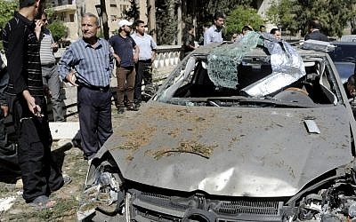 This photo released by the Syrian official news agency SANA, shows Syrians inspecting a damaged car at the scene of a car bomb exploded in the capital's western neighborhood of Mazzeh, in Damascus, Syria, Monday, April. 29, 2013 (photo credit: AP/SANA)