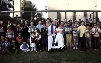 Canon White with children outside his Baghdad church before prayers in February (YouTube screenshot) Canon White with children outside his Baghdad church before prayers in February (YouTube screenshot)