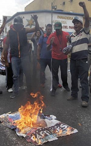 Government "Chavista" supporters burn an election poster of opposition presidential candidate Henrique Capriles in Los Teques, on the outskirts of Caracas, Venezuela, on Tuesday, April 16, 2013. (photo credit: AP Photo/Ariana Cubillos)