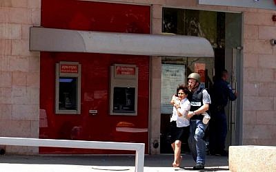 Miriam Cohen, who was held hostage by gunman Itamar Alon in the Bank Hapoalim branch in Beersheba on Monday, is escorted out of the bank after Alon, who killed four people, took his own life (photo credit: Dudu Greenspan/Flash90)