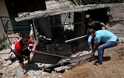 Lebanese men remove debris from their home, which was damaged due to rockets fired by Syrian rebels, according to villagers, in the northeast Lebanese village of Hermel on Wednesday. (photo credit: AP/Hussein Malla)