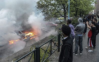 Bystanders watch a row of burning cars in the Stockholm suburb of Rinkeby after youths rioted in several different suburbs around Stockholm for a fourth consecutive night, late Thursday May 23. (Photo credit: AP Photo/Scanpix, Fredrik Sandberg)