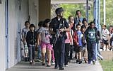 A Santa Monica police officer leads children on a field trip from Citizens of the World Charter School in Los Angeles out of Santa Monica College, where they had gone for a planetarium show, following a shooting in the area in Santa Monica, California on Friday. (photo credit: AP Photo/Reed Saxon)