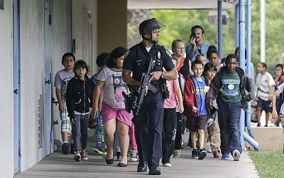 A Santa Monica police officer leads children on a field trip from Citizens of the World Charter School in Los Angeles out of Santa Monica College, where they had gone for a planetarium show, following a shooting in the area in Santa Monica, California on Friday. (photo credit: AP Photo/Reed Saxon)